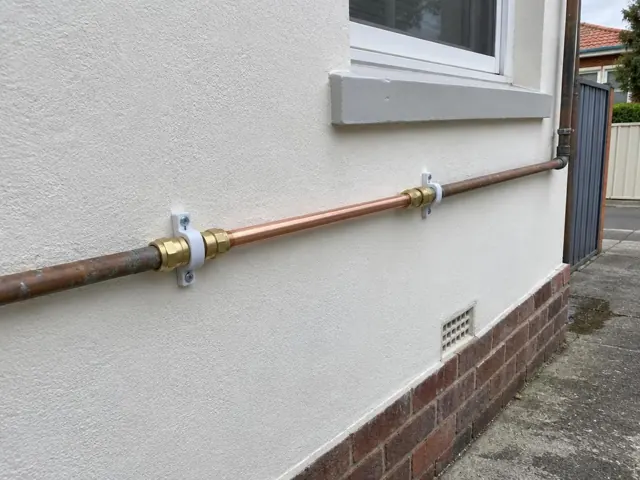 Copper water pipe repair on an exterior stucco wall below a window in Mascot